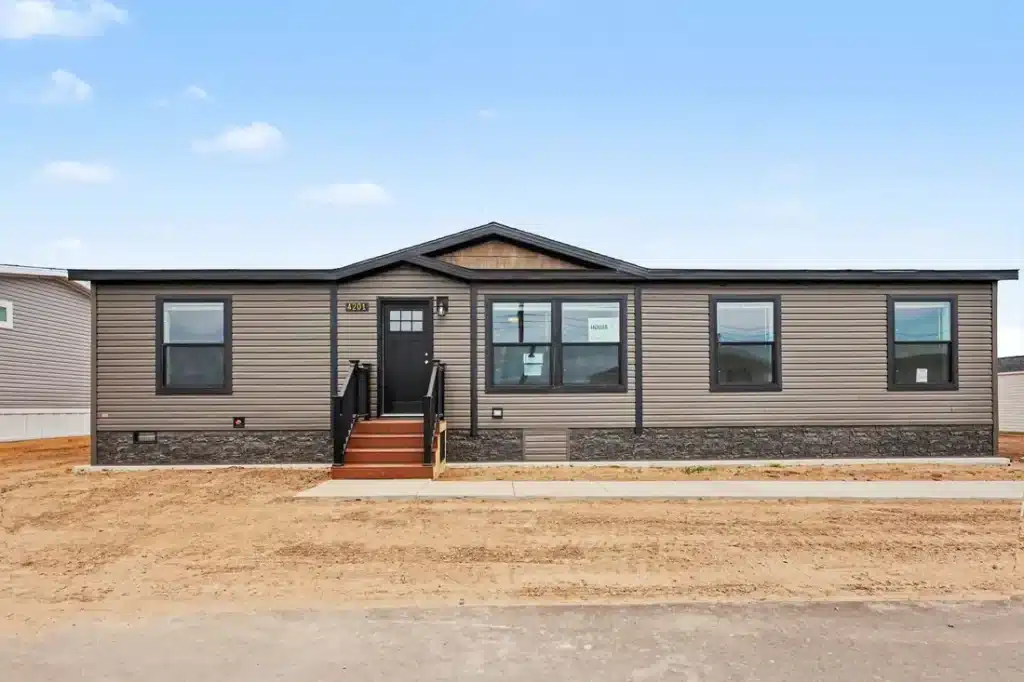 Front exterior of a new brown manufactured home with stone skirting