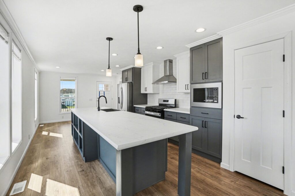 Kitchen with gray island, white cabinets and pendant lights in a new manufactured home at 4198 Shalimar Dr in Allendale, MI