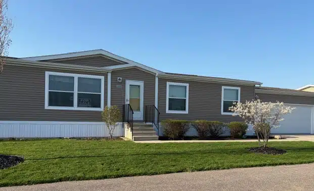 Front exterior of a pre-owned tan manufactured home with landscaping at 4393 Twilight Way near Holland, MI