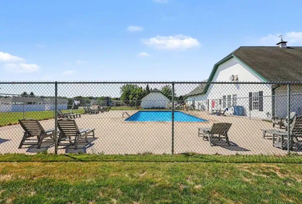 Fenced outdoor swimming pool with lounge chairs beside the clubhouse at the manufactured home community