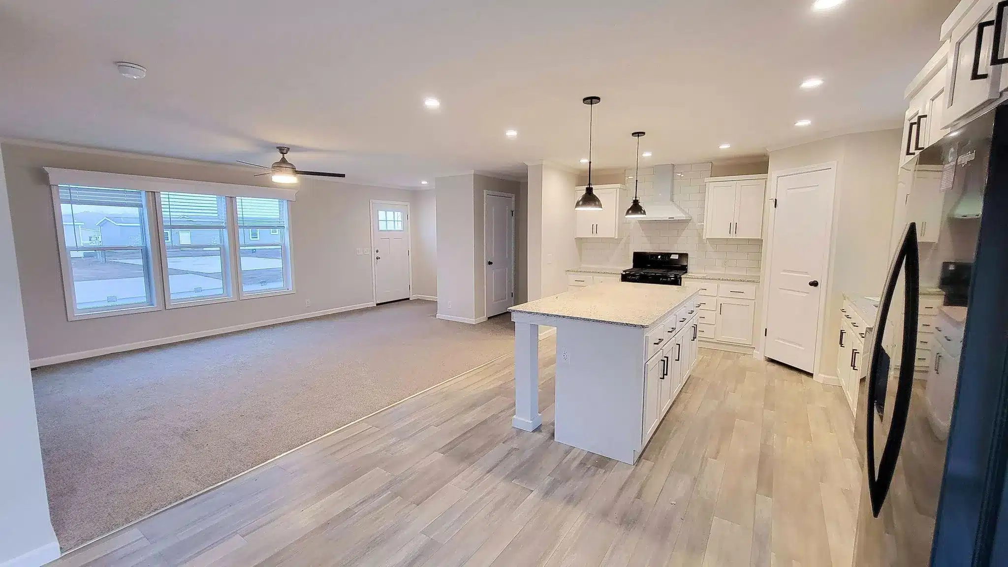 Open living room and white kitchen with island and pendant lights in a new manufactured home in Allendale, MI